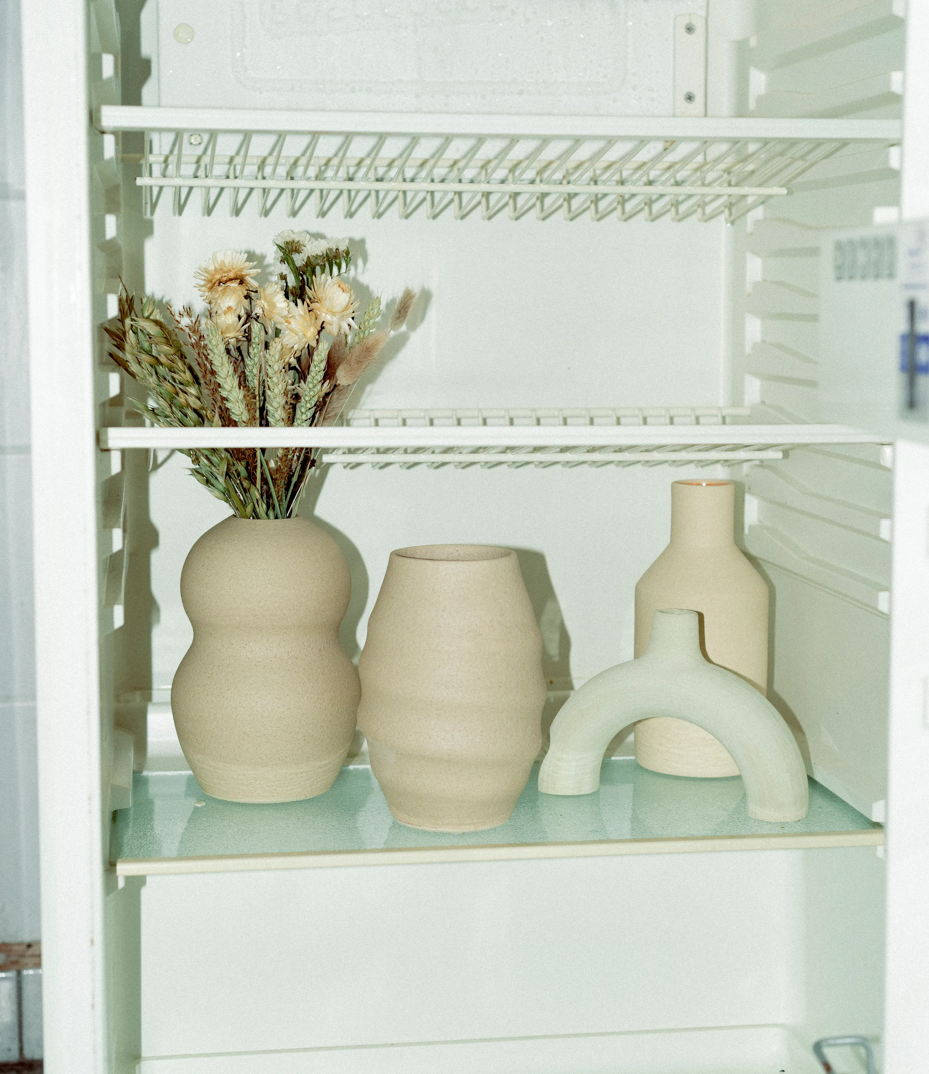 A selection of Ocactuu's and Nova Casa Atlantica's items showcased in a vintage fridge with dried flowers. All of the products are light and beige.
