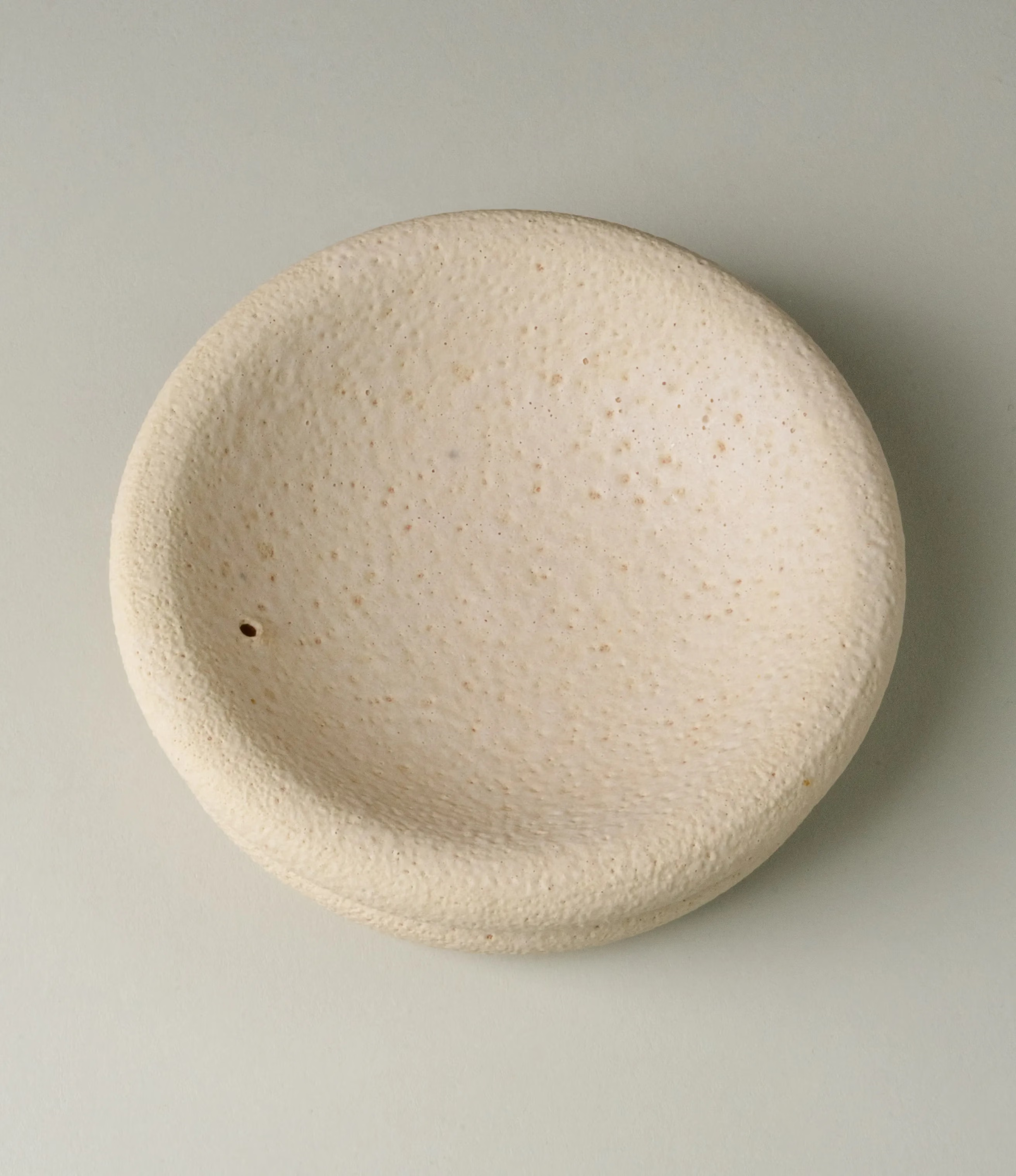 Lyot Incense Holder designed by Ocactuu has a sand texture and comes in a light nude color. The rounded plate has the place for your incense close to the edge of it. The picture captures the product from the top.