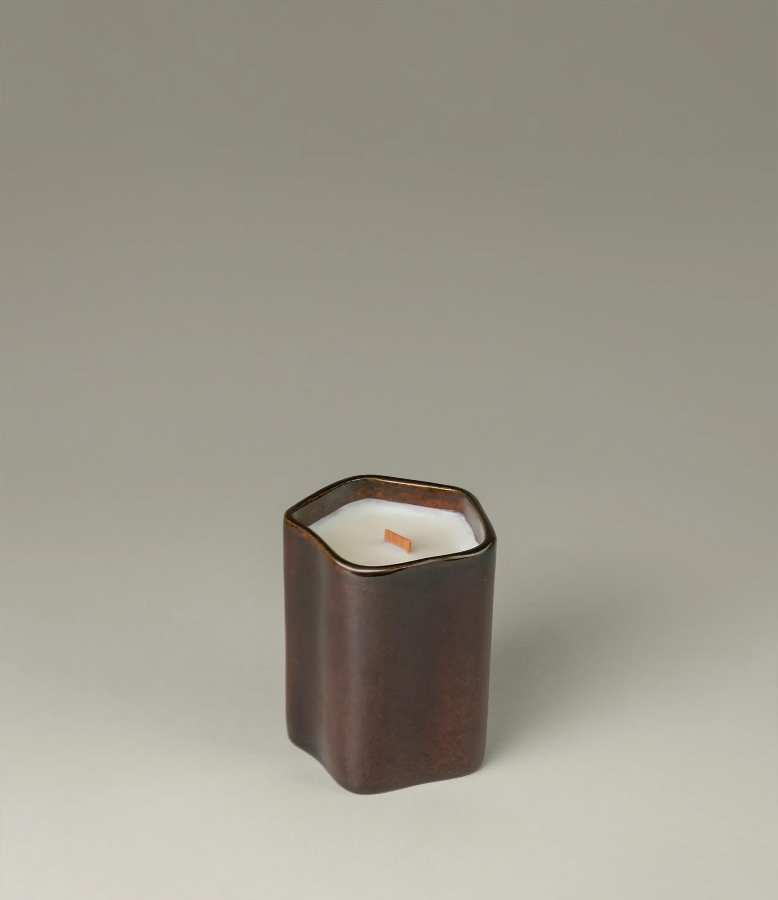 A scented Wax Candle designed by Ocactuu. The candle has a peach scent and it comes in a glossy dark brown ceramic. The material has a subtle spotted texture. The candle wick is made of wood for a more natural feeling.  