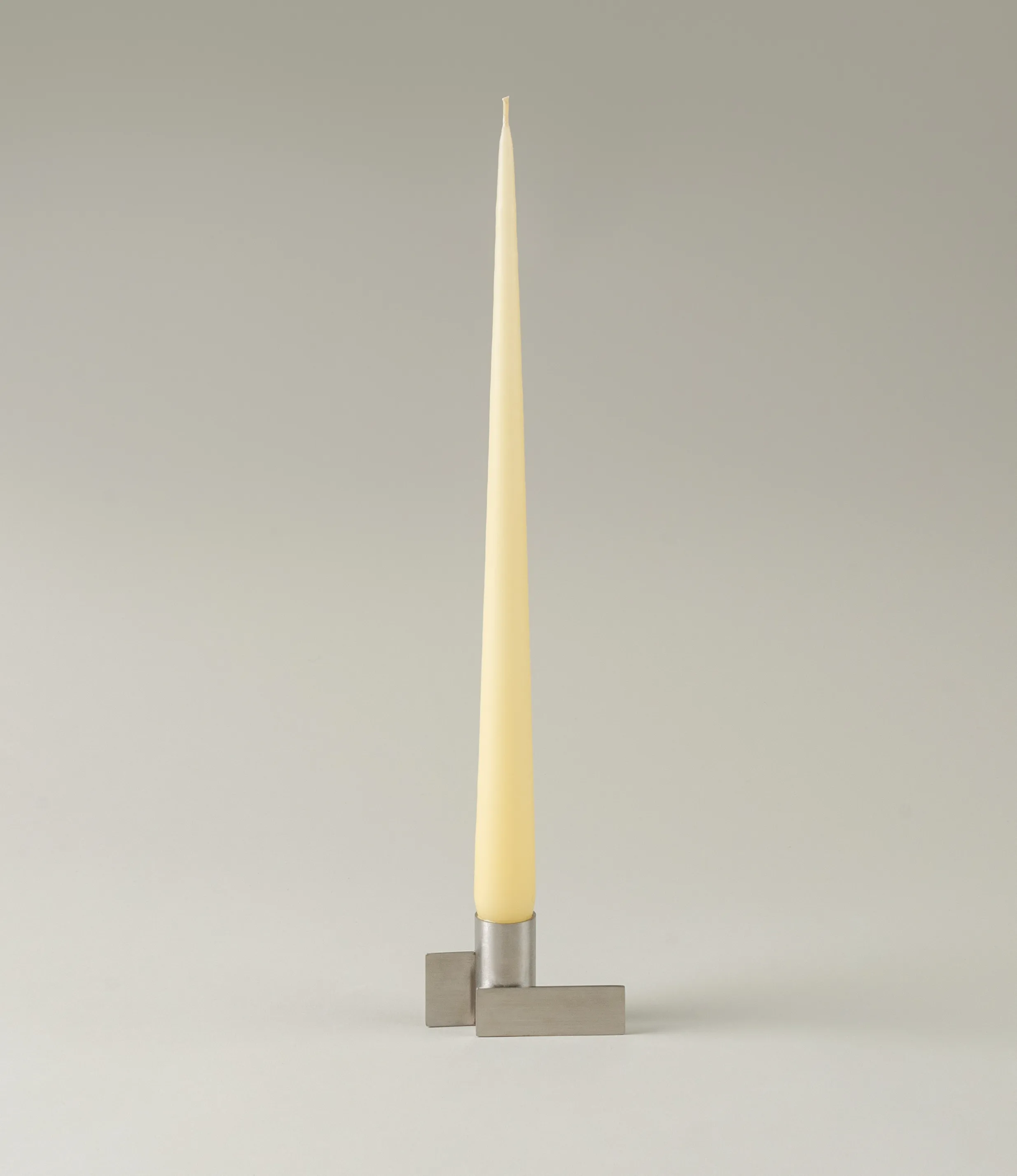 Ester&Erik Taper Candle coming in a Buttermilk shade. The product is showcased in a stainless steel Icon Candleholder from Stences.
